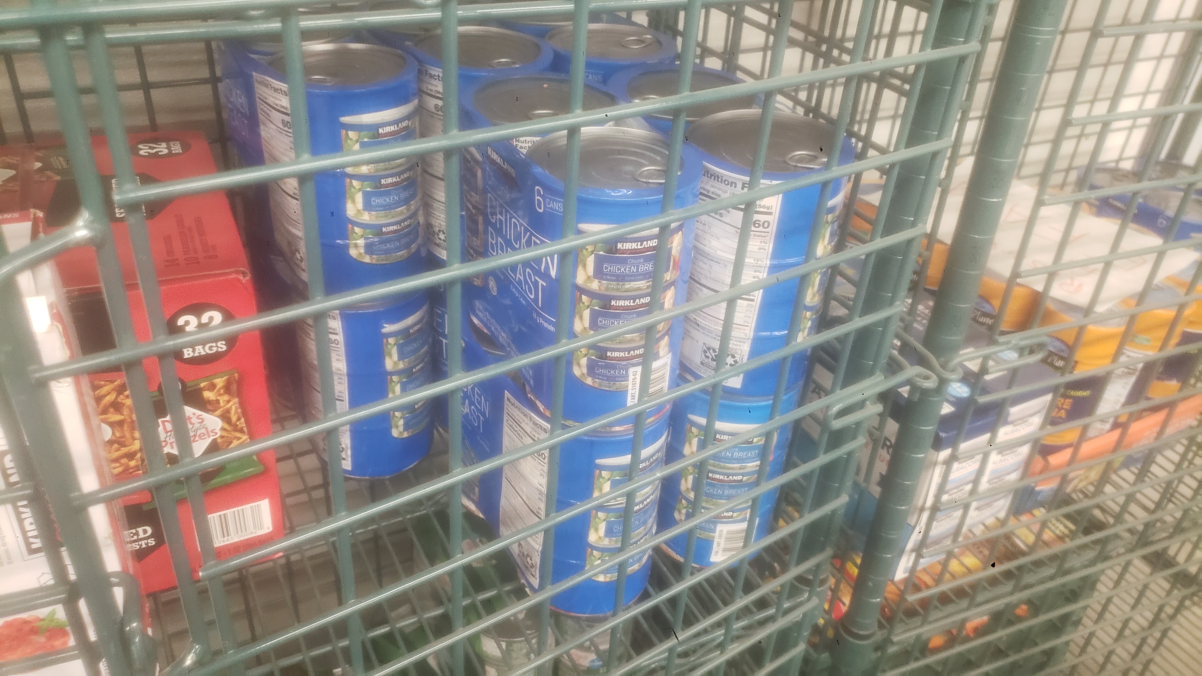 Canned chicken and bags of pretzels in a cage shelf.